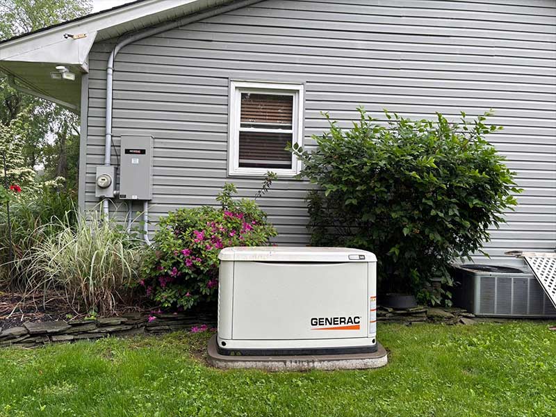 Standby generator on a concrete pad beside a home, with a transfer switch mounted next to the electric meter
